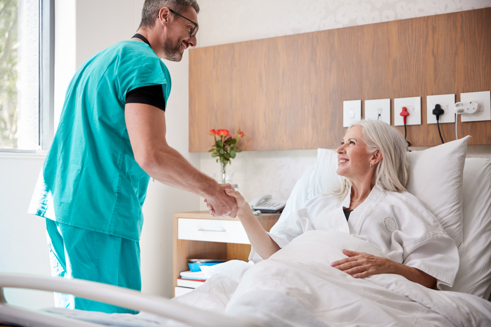 Médico apertando mão de paciente deitada em cama de hospital.